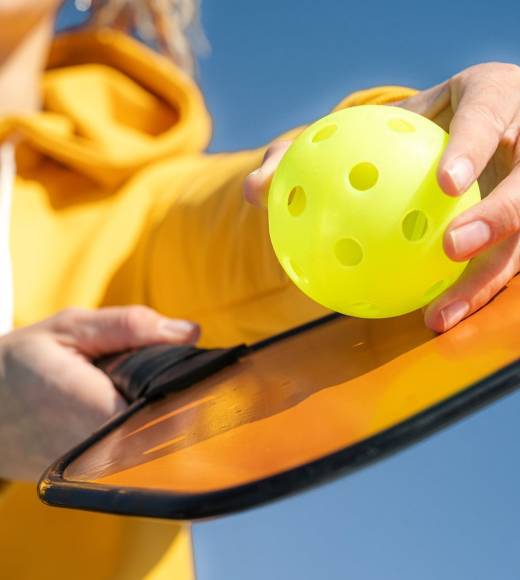 Pickleball paddle and yellow ball close up, woman playing pickleball game, hitting pickleball yellow ball with paddle, outdoor sport leisure activity