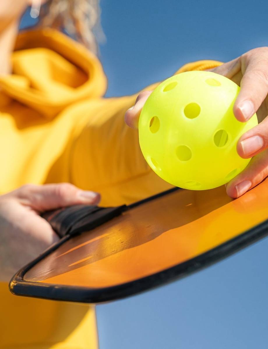 Pickleball paddle and yellow ball close up, woman playing pickleball game, hitting pickleball yellow ball with paddle, outdoor sport leisure activity